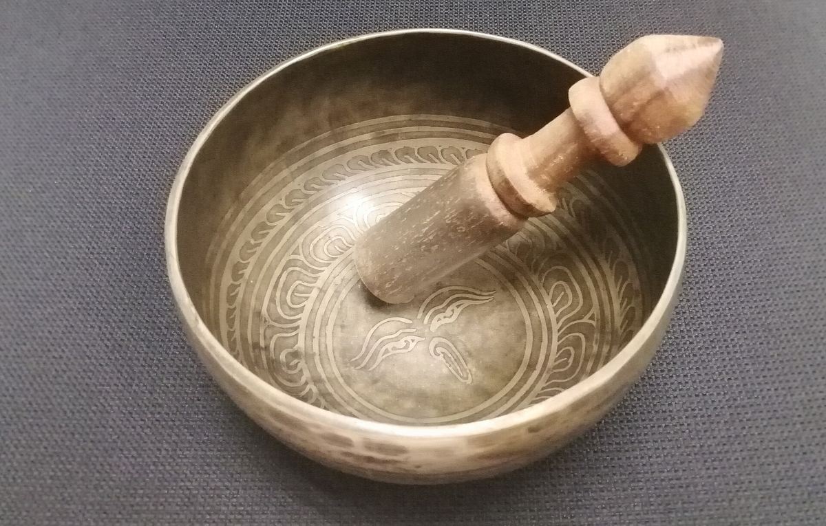 Eine Klangschale aus Metall mit Klöppel auf einer Unterlage
